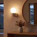 Travertine ledge and frosted glass orb wall sconce beside a round mirror in an entry hall