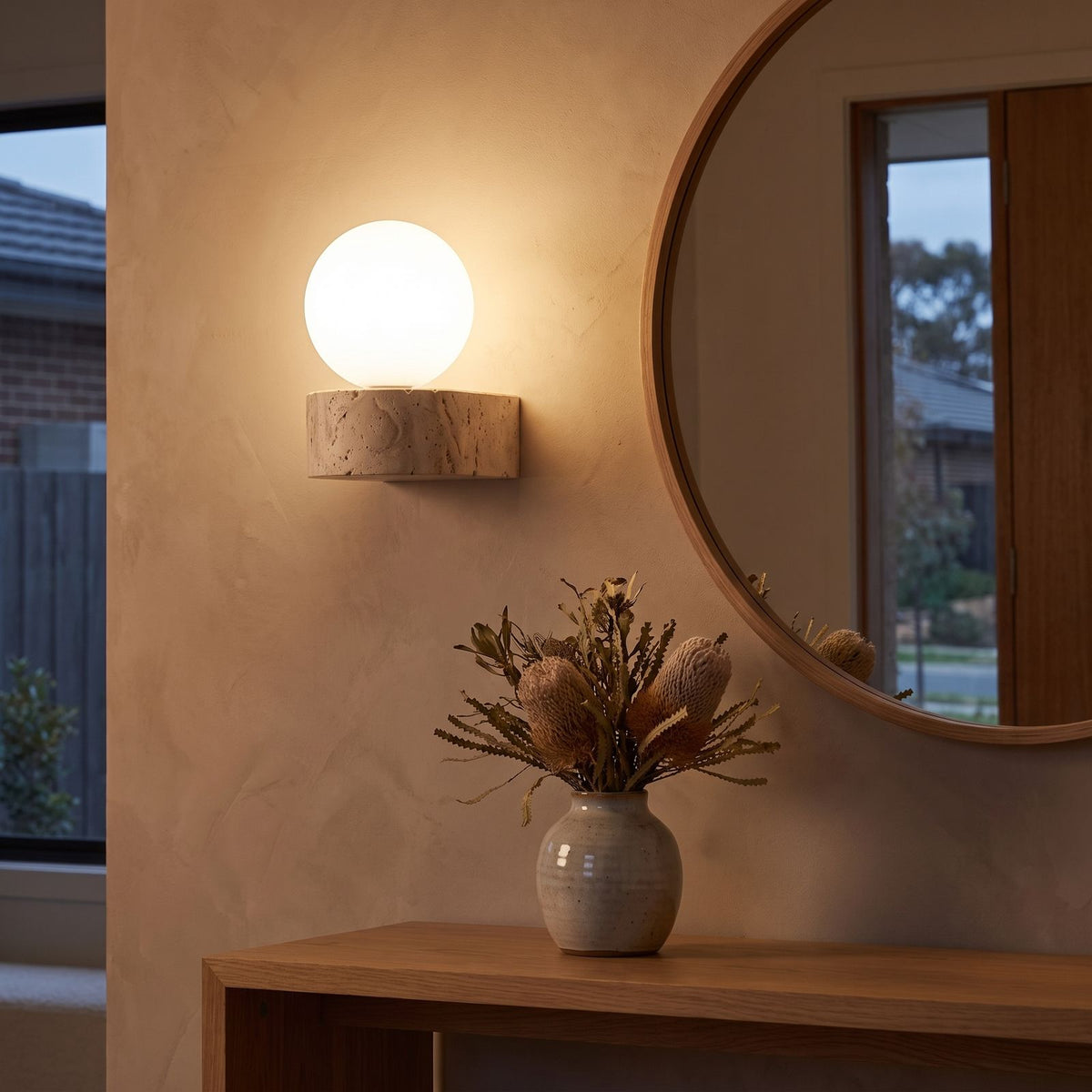 Travertine ledge and frosted glass orb wall sconce beside a round mirror in an entry hall