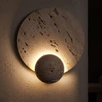 Travertine Pattern Marble Disc and Orb Wall Light glowing on a plaster wall at night