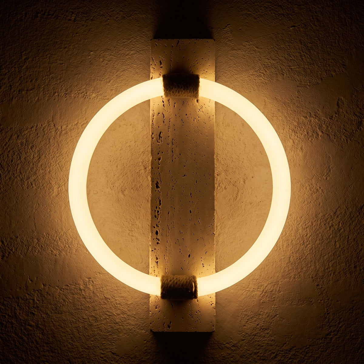 Travertine Plank and LED Ring Wall Light glowing on a plaster wall at night