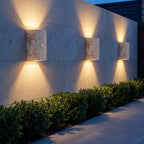 Three Travertine Stone Outdoor Up Down Wall Lights along a stone garden wall