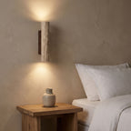 Travertine Tube Up Down Wall Light beside a bed at night