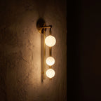 Triple Frosted Glass Orb Vertical Wall Light glowing on a plaster wall at night