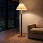 Turned wood floor lamp with pleated shade behind a sofa at night
