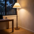 Turned wood floor lamp with pleated shade in a home office corner beside a desk
