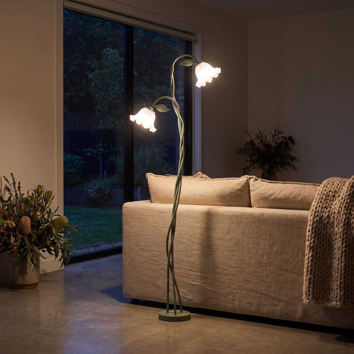 Green stem flower shade floor lamp behind a sofa at night