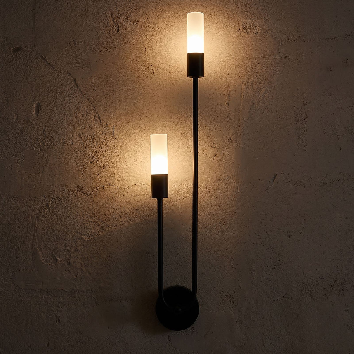 Two-Arm Iron and Acrylic Tube Wall Light glowing on a plaster wall at night