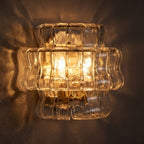 Two Tier Fluted Glass Brass Wall Sconce glowing on a plaster wall at night