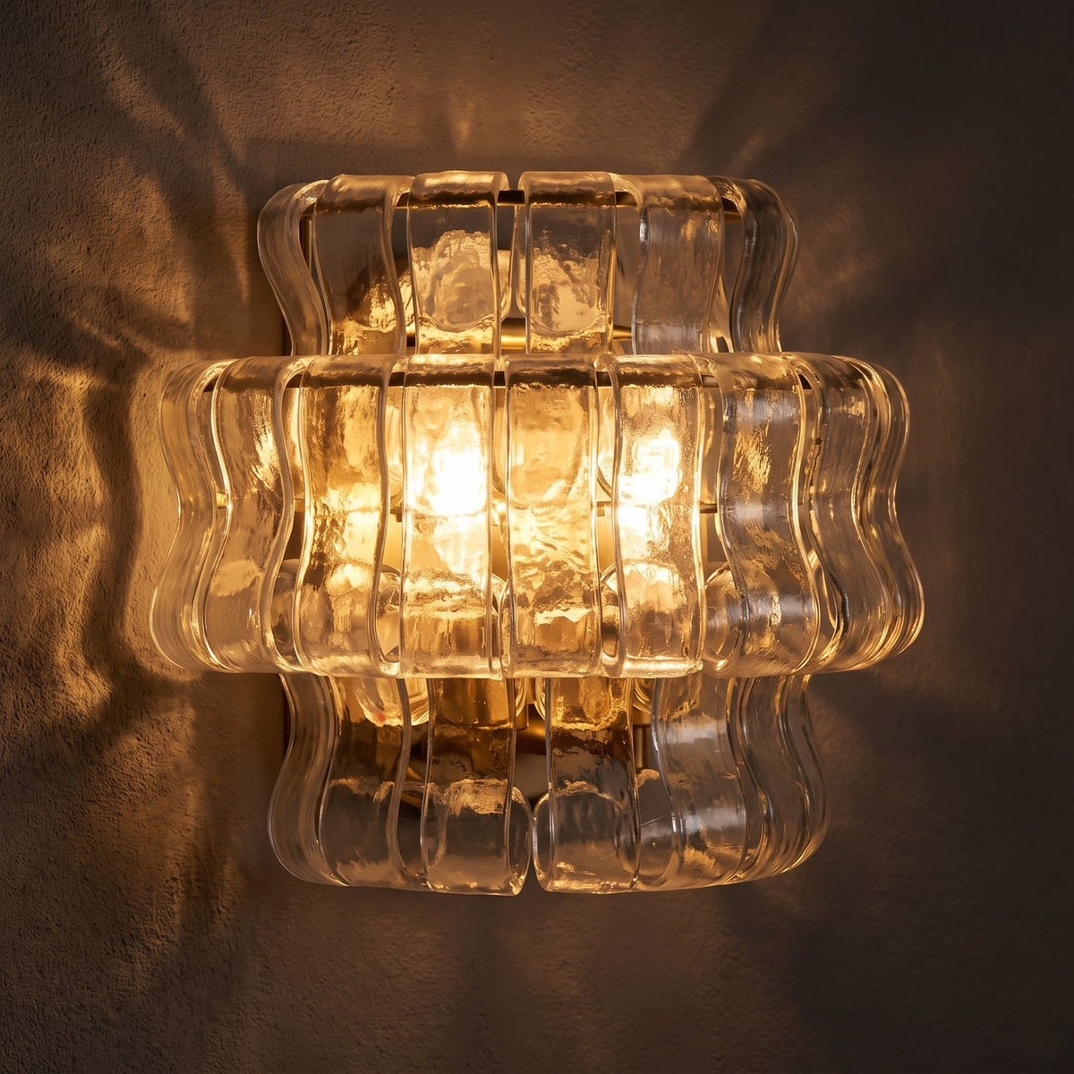 Two Tier Fluted Glass Brass Wall Sconce glowing on a plaster wall at night