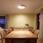 Ultra thin LED oyster ceiling light lighting a timber dining table in a country farmhouse at dusk