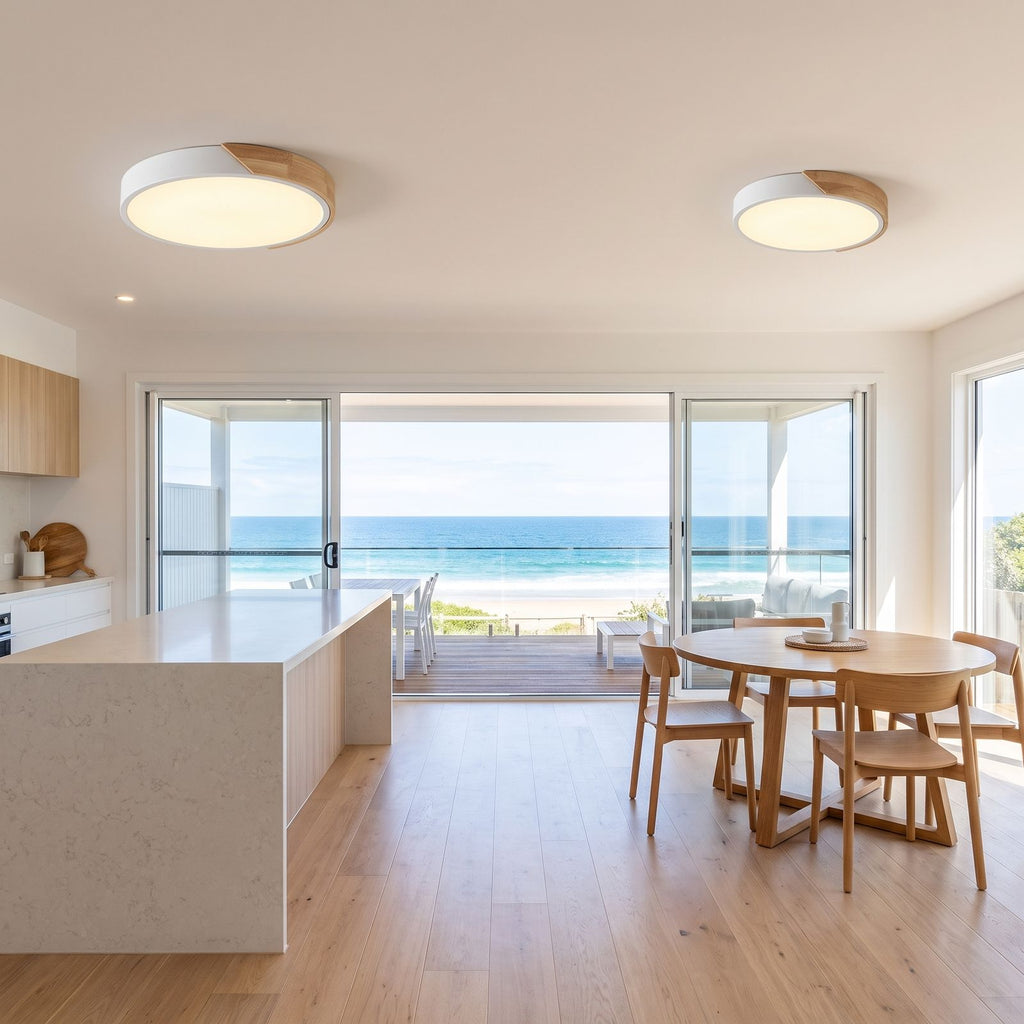 Two ultra thin LED oyster ceiling lights over the kitchen bench and dining table of an open plan beach house