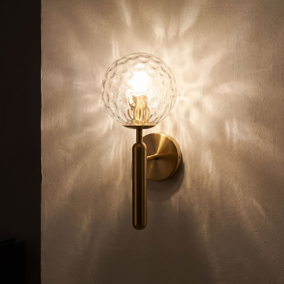 Upturned Glass Globe Wall Light glowing on a plaster wall at night