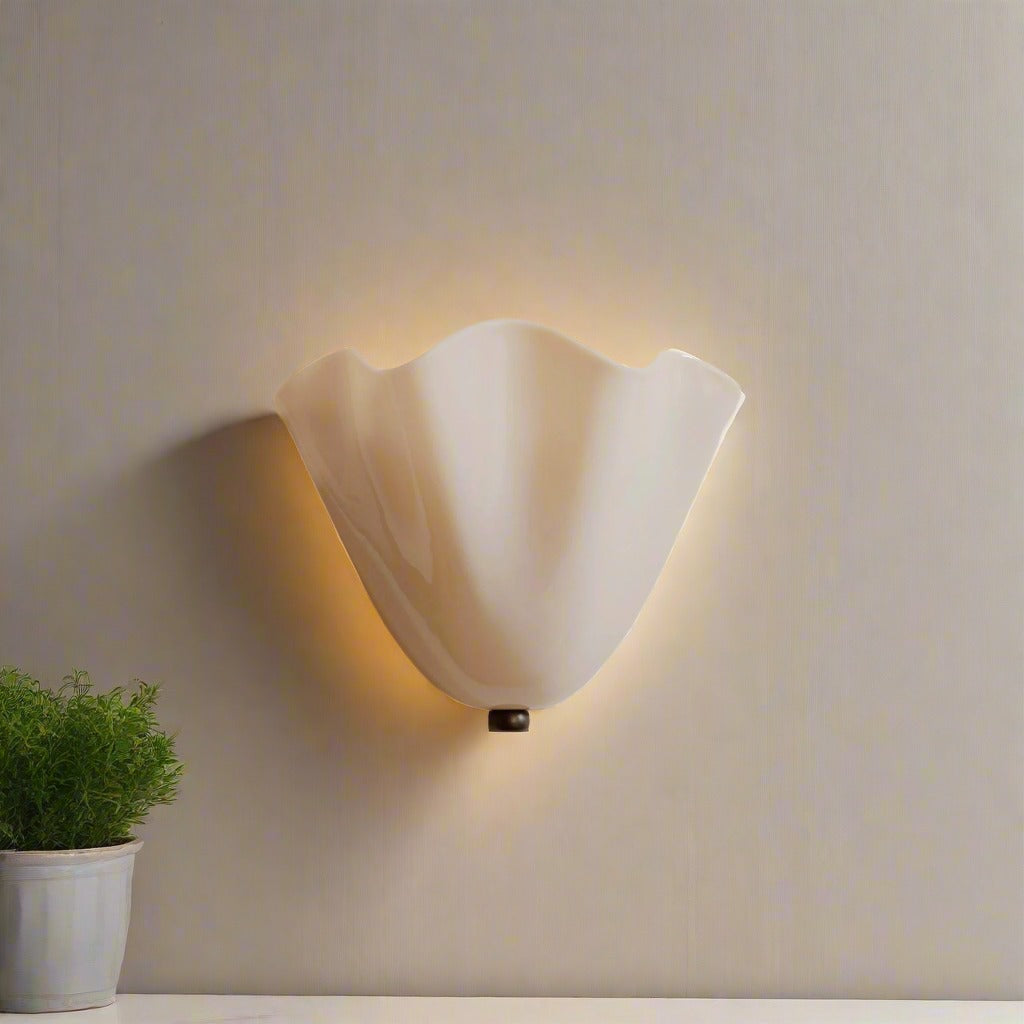 Beige glass shell wall light glowing beside a bed