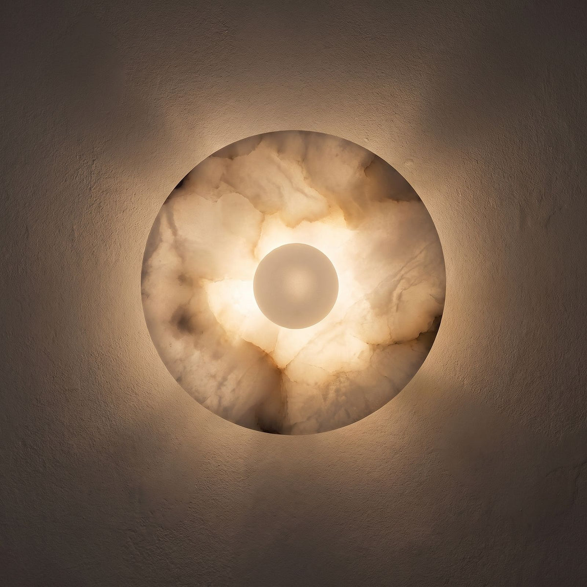 White Alabaster Halo Wall Light glowing on a plaster wall at night