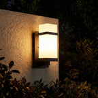 White Glass Black Iron Outdoor Wall Light glowing on a garden wall at night