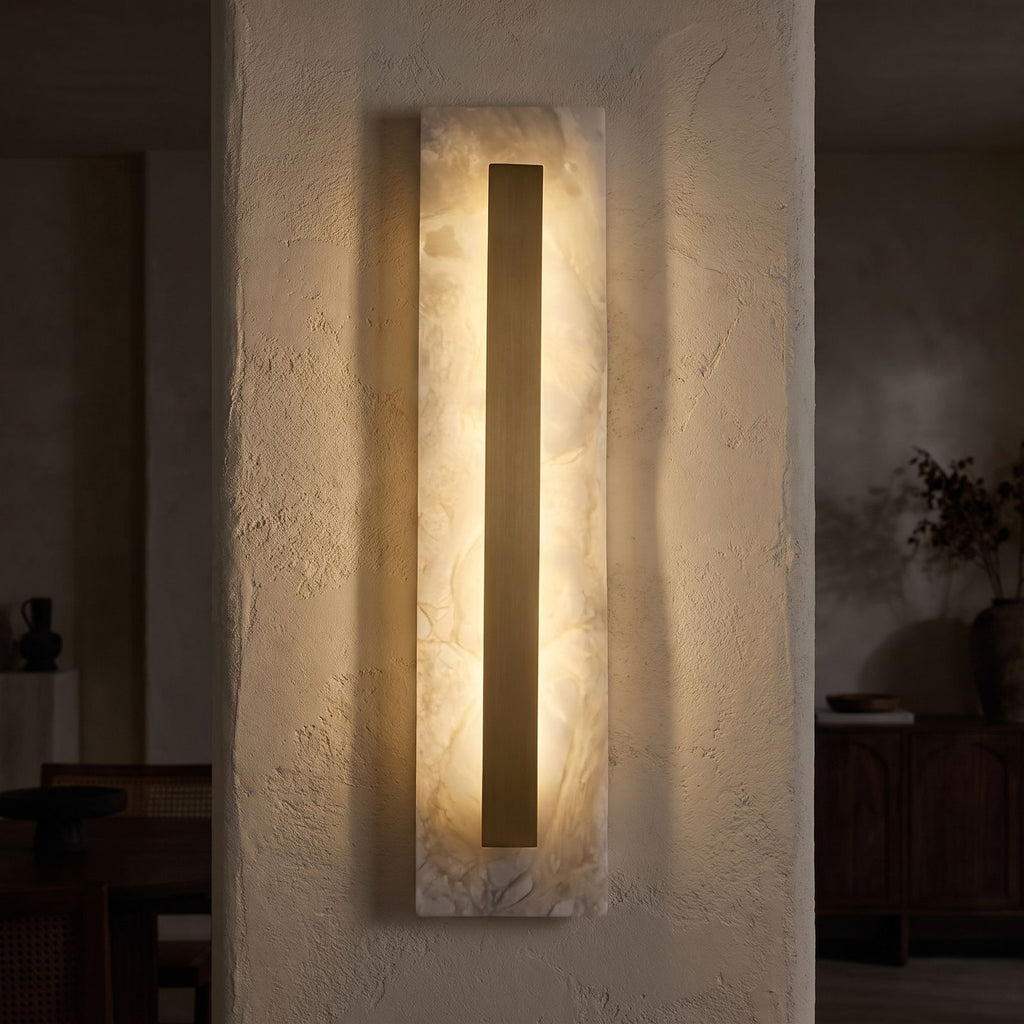 Wide Alabaster Panel Brass Wall Light glowing on a plaster wall at night