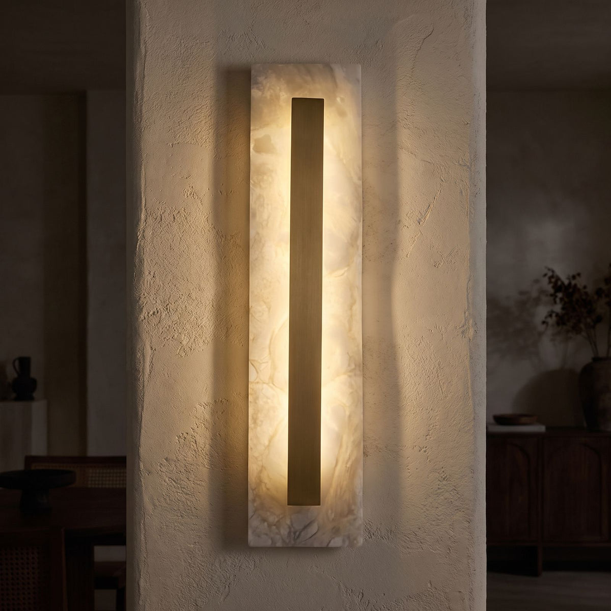 Wide Alabaster Panel Brass Wall Light glowing on a plaster wall at night