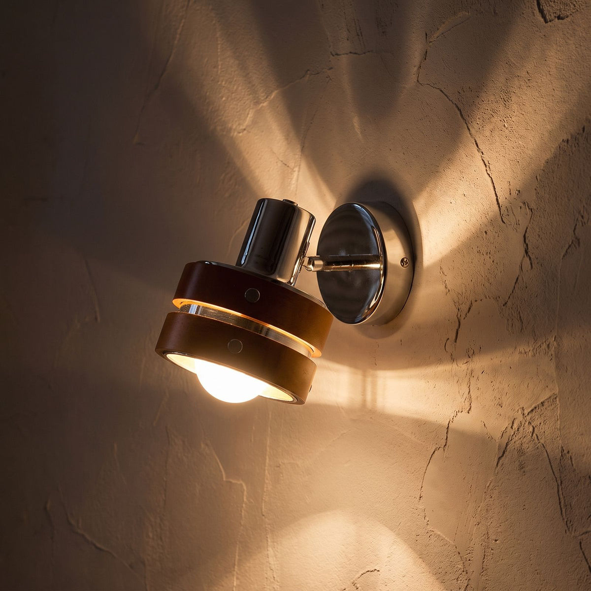 Wood Cylinder Shade Iron Disc Wall Light glowing on a plaster wall at night