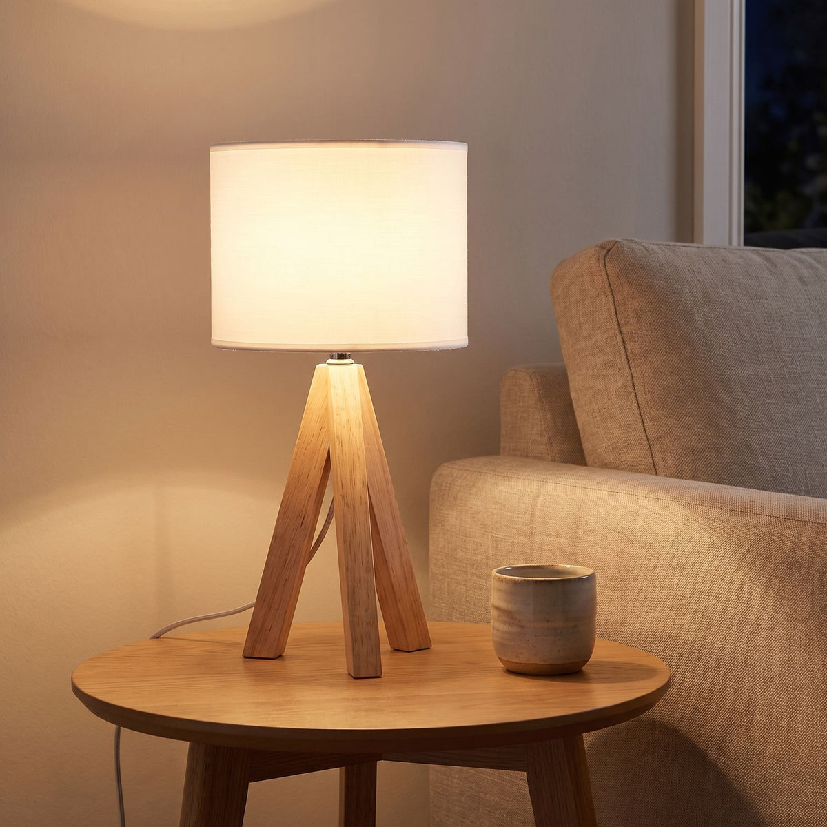 Wood tripod drum shade table lamp on a side table beside a sofa
