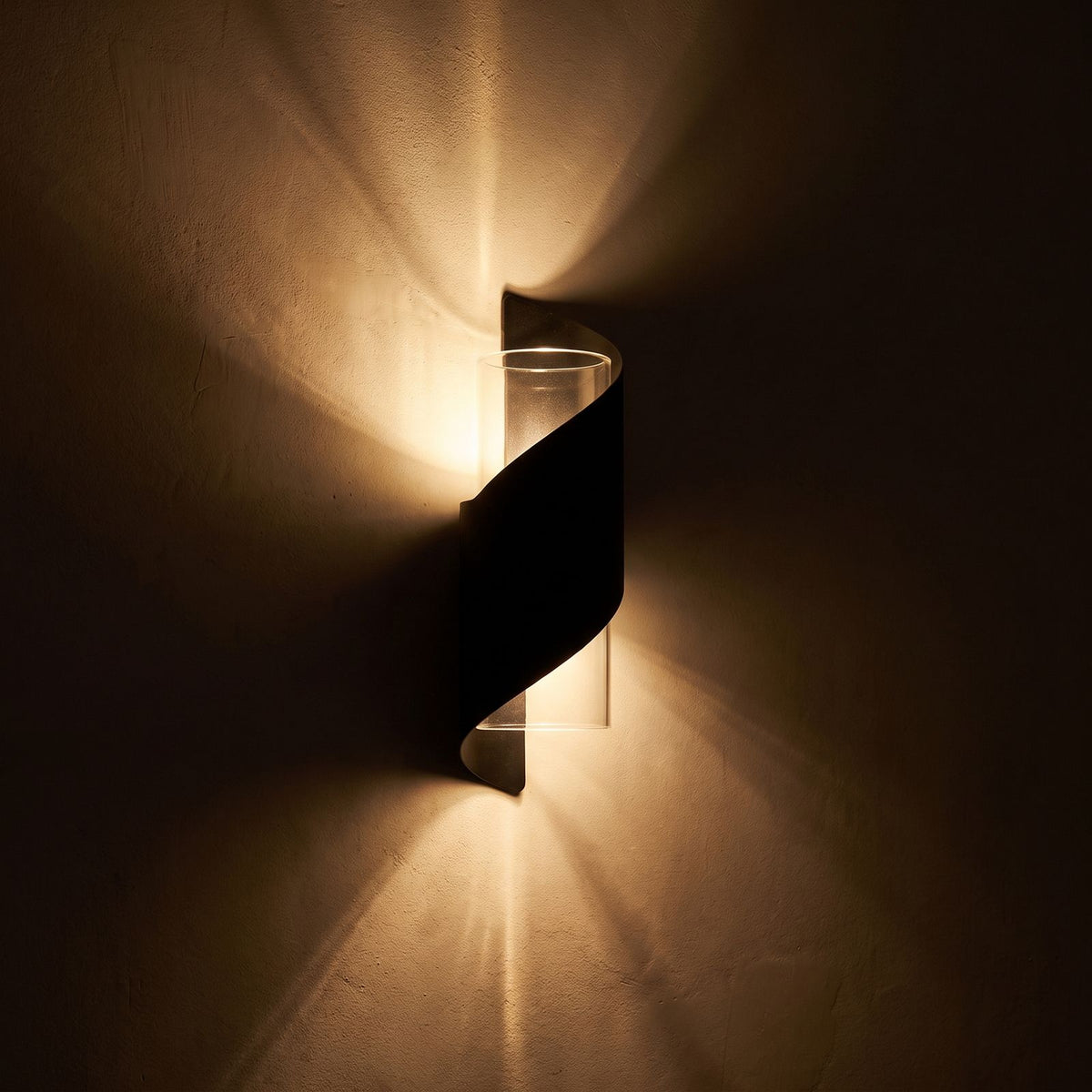 Wrap Around Aluminium and Glass Up Down Wall Light glowing on a plaster wall at night